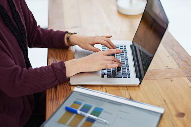 Produtividade na ponta dos dedos Foto recortada de uma mulher não identificável usando seu laptop no escritório