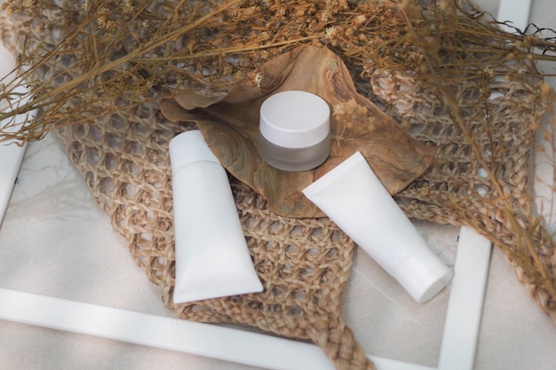 Foto produto branco dos recipientes cosméticos da garrafa com bolsas tecidas, flor seca, folha.