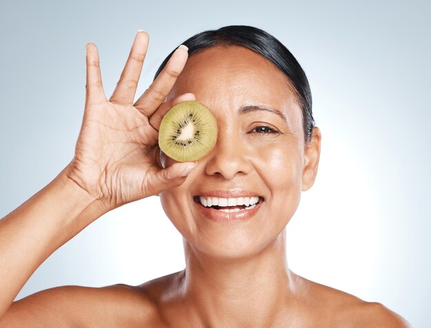 Produto de beleza kiwi e retrato de mulher com sorriso no rosto para desintoxicação facial de vitamina c e feliz no fundo do estúdio Cuidados com a pele saudáveis, bem-estar e sustentabilidade na limpeza de luxo de frutas nos olhos