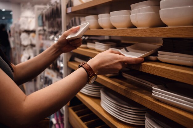 Produtos comparados pelo cliente do rack na loja. Jovem mulher escolhendo louça