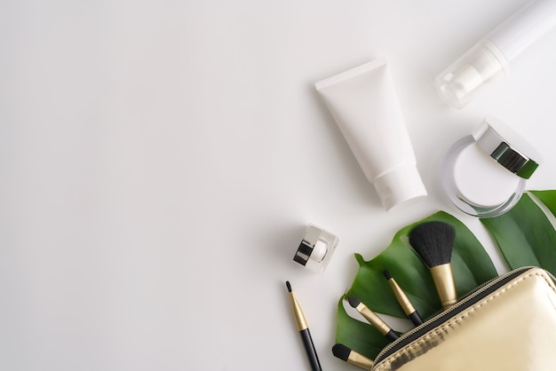 Produtos cosméticos brancos e folhas verdes sobre fundo branco.