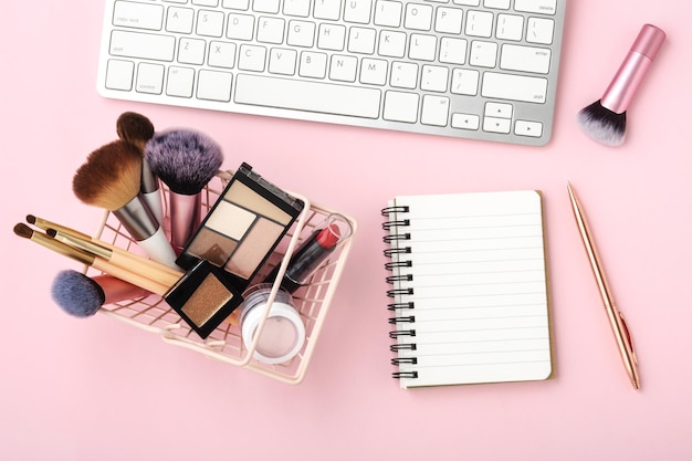 Foto produtos cosméticos de maquiagem com caderno e teclado em mesa rosa pastel