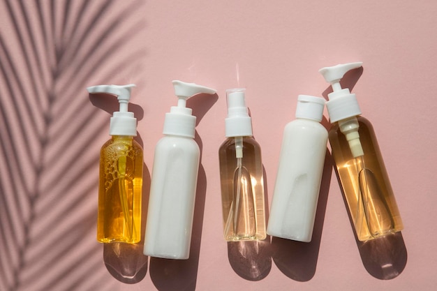 Produtos cosméticos em garrafas em um fundo rosa com sombra de folha de palmeira tropical