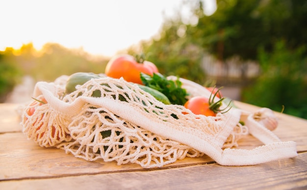 Produtos de legumes frescos e suculentos em um saco de compras reutilizável um saco de corda feito de materiais reciclados em uma mesa de madeira no jardim Vegetarianismo Sem plástico Estilo de vida ecológico