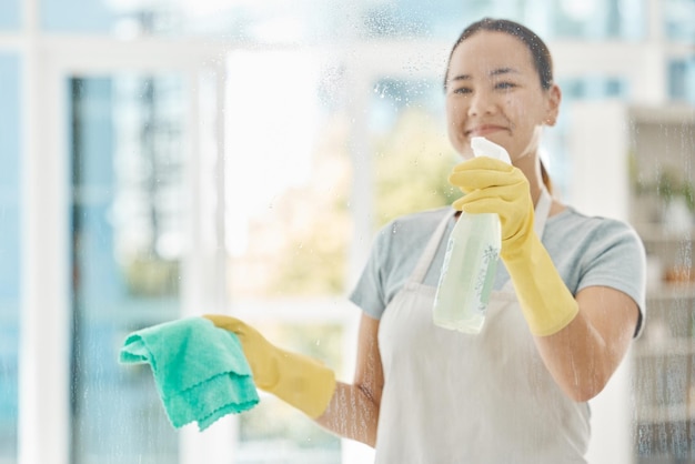 Produtos de limpeza e mulher feliz limpando as janelas com pano detergente e luvas Limpeza de empregada doméstica ou trabalhadora doméstica lavando a poeira e as bactérias do vidro em um prédio de apartamentos