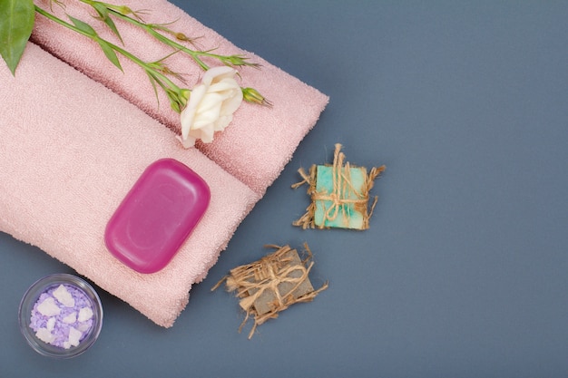 Produtos de spa para cuidados faciais e corporais. sal marinho natural, sabonete caseiro e toalhas cor de rosa com flores em fundo cinza. conceito de spa e cuidados corporais. vista do topo.