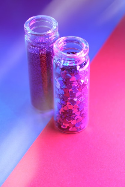 Produtos em pó de glitter colorido neon Closeup em dois frascos de frascos com vários glitter em cores rosa roxas e vibrantes em papel dividido