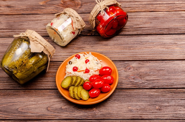 Produtos lácteos fermentados saborosos caseiros em placas - chucrute, tomate, picles, na mesa de madeira, copie o espaço. postura plana.