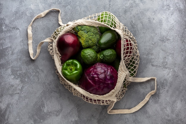 Produtos verdes e roxos em uma sacola ecológica em um fundo cinza