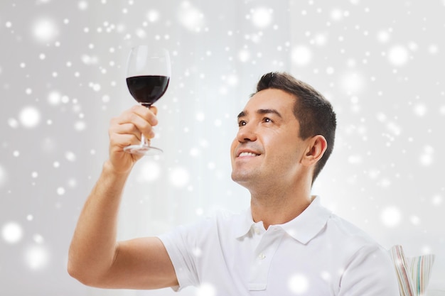 profesión, bebidas, ocio y concepto de la gente - hombre feliz bebiendo vino tinto de vidrio en casa sobre el efecto de la nieve