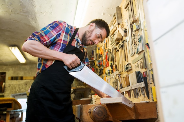 Profesión, carpintería, carpintería y concepto de personas: carpintero que trabaja con sierra y tablones de madera en el taller