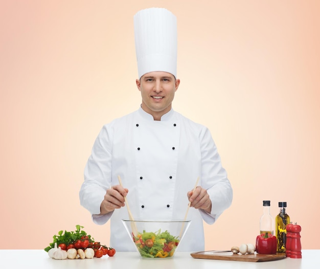 Profesión, vegetariano, comida y concepto de personas - feliz chef masculino cocinando ensalada de verduras sobre fondo beige