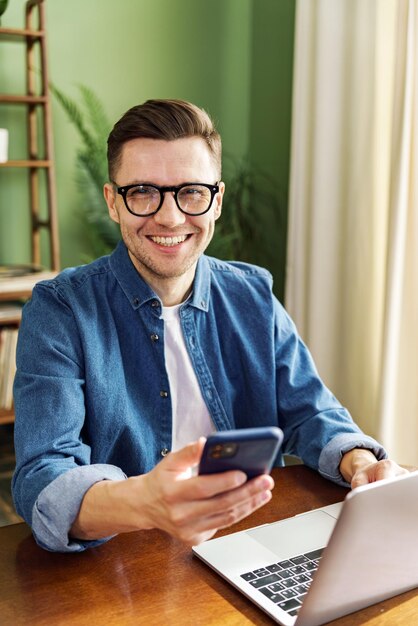 Un profesional alegre multitarea con un teléfono inteligente y una computadora portátil su sonrisa refleja el