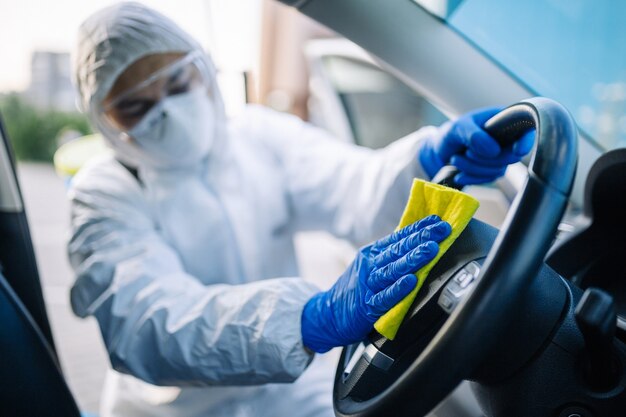 Profesional de desinfección limpia un volante de un coche