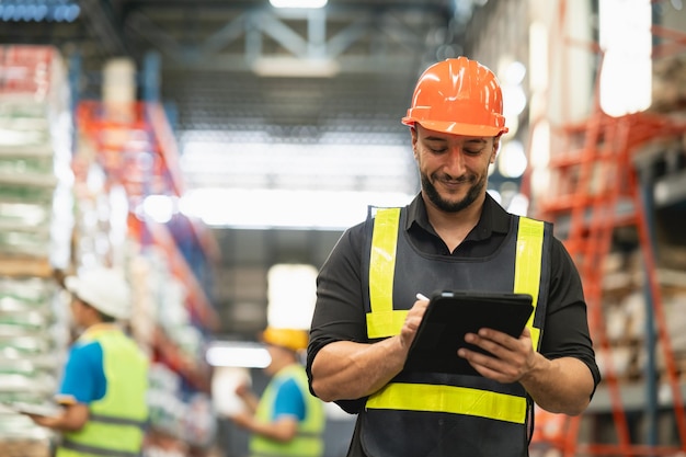 Profesional gerente empleado sonrisa usando tableta comprobación de stock trabajando en el almacén Trabajador con ropa de alta visibilidad y un casco de casco y comprobación y conteo de cajas de mercancías entrega