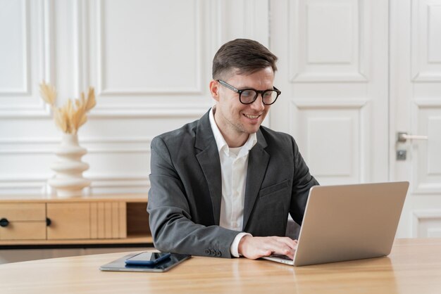 Un profesional de negocios con gafas trabajando atentamente en una computadora portátil muestra productividad y concentración en un espacio de oficina brillante