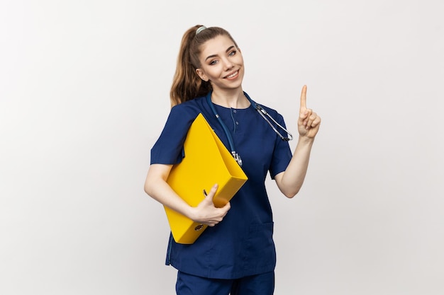 Un profesional de la salud vestido con ropa médica azul que sostiene documentos en un entorno de estudio blanco Foto en blanco para una empresa de publicidad sobre medicina
