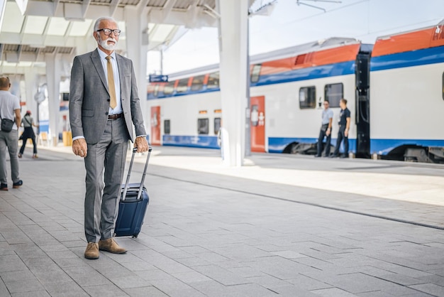 Profesional senior con equipaje de pie y esperando en la plataforma de la estación de metro o tren