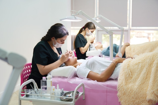 Profesionales que trabajan con clientes en salón de belleza mujer acostada en entrenador cosmetológico durante