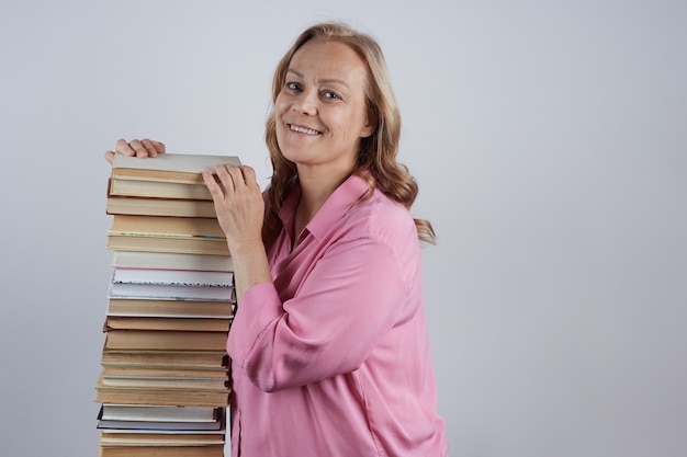 Profesor alegre en una blusa rosa se encuentra junto a una gran pila de retrato de libros