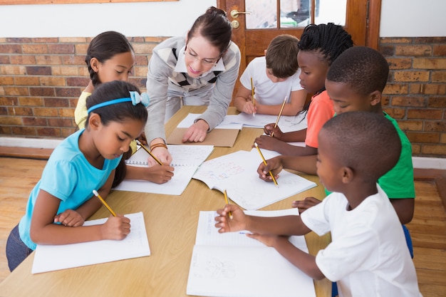 Profesor y alumnos trabajando en el escritorio juntos en la escuela primaria