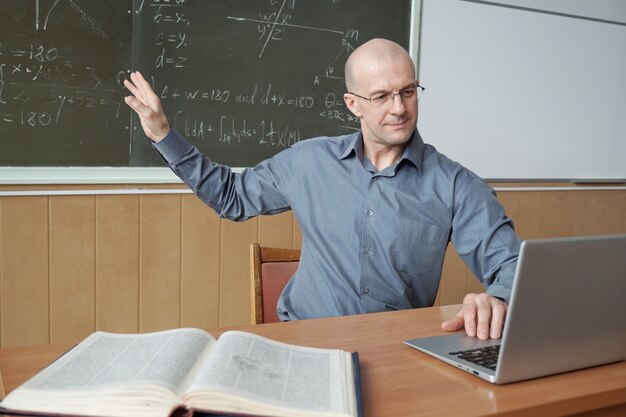 Profesor apuntando a la pizarra con fórmulas delante de la computadora portátil