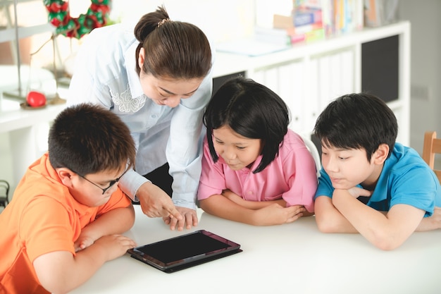 Profesor asiático y niños entreteniéndose con tableta digital