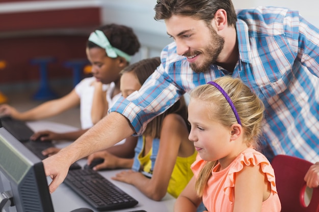 Profesor ayudando a colegialas en el aprendizaje de la computadora