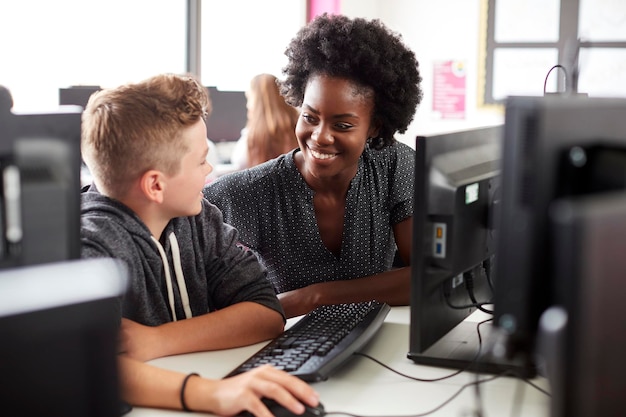 Profesor ayudando a estudiante de secundaria masculino trabajando en pantalla en clase de computación