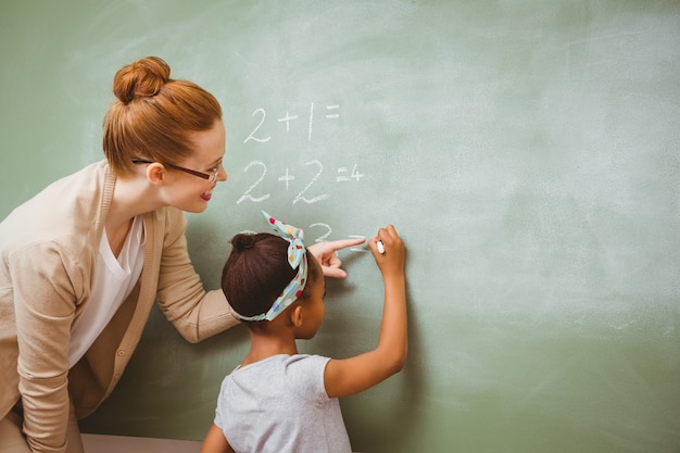 Profesor ayudando a la niña a escribir en la pizarra en el aula