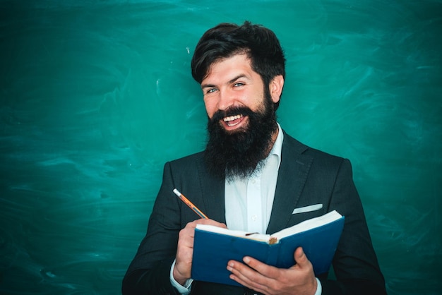 Profesor barbudo en la lección de la escuela en los escritorios en el aula Educación Joven maestro cerca de la pizarra en el aula de la escuela Profesor amable en el aula cerca del escritorio de la pizarra