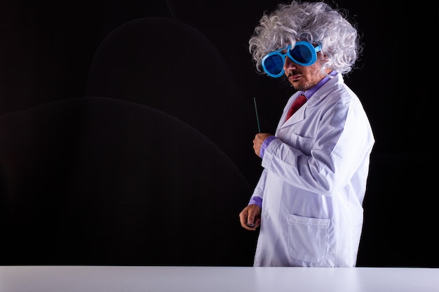 Profesor de ciencias loco en bata blanca con el pelo descuidado en gafas divertidas sosteniendo una varita para apuntar a la pizarra