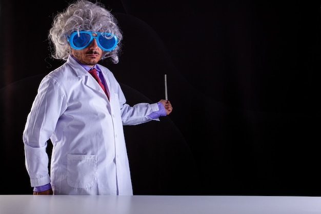 Profesor de ciencias loco en bata blanca con el pelo descuidado en gafas divertidas sosteniendo una varita para apuntar a la pizarra