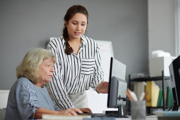 Profesor de clase de formación informática trabajando con una mujer mayor