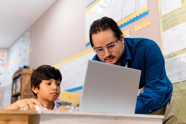 Profesor y colegial varones diversos usando una computadora portátil en la clase de escuela primaria