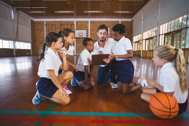 Profesor de deporte y niños de la escuela discutiendo en el portapapeles en la cancha de baloncesto