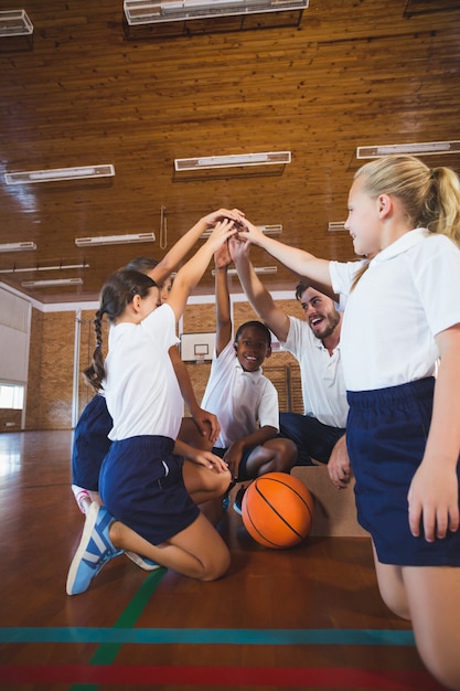 Profesor de deportes y niños de la escuela formando una pila de manos en la cancha de baloncesto