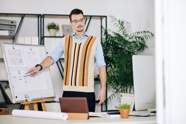 Profesor de diseño de UX y UI apuntando a diseños en la pizarra cuando imparte clases en línea para estudiantes