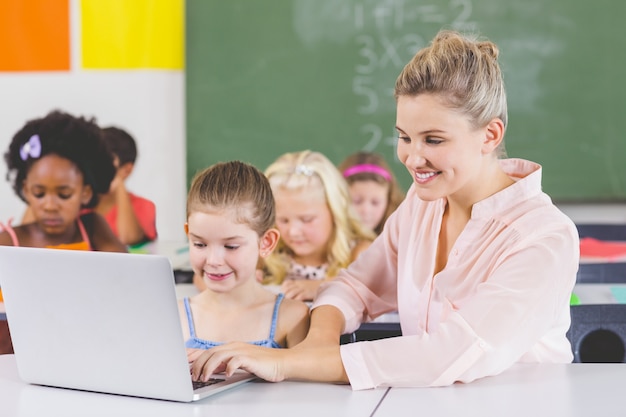 Profesor enseñando colegiala en la computadora portátil