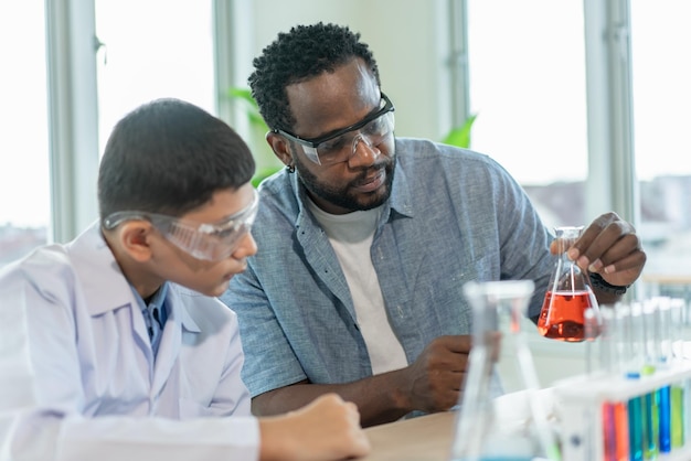 Profesor enseñando a un estudiante que estudia química y mira el tubo en la clase de ciencias elementales