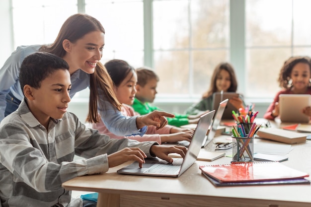 Profesor enseñando a niños de escuela diversa usando una computadora portátil en el aula