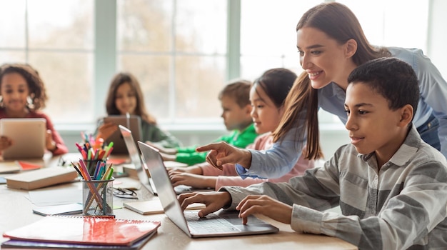 Profesor enseñando a niños de escuela diversa usando una computadora portátil en el aula