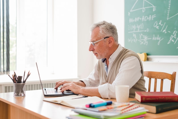 Foto profesor envejecido trabajando en la computadora portátil en el aula