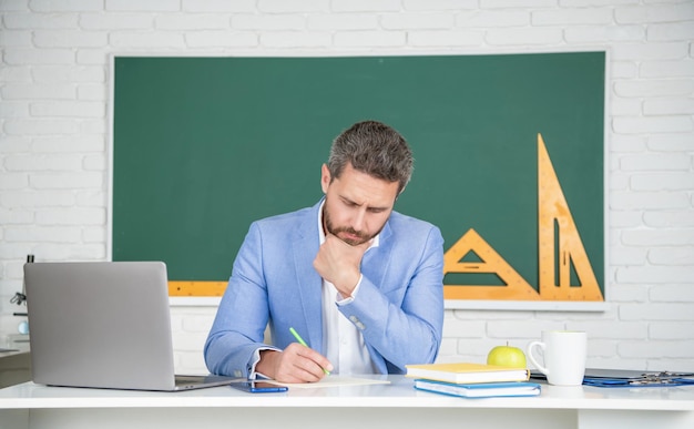 Profesor de escuela en aula con laptop en pizarra