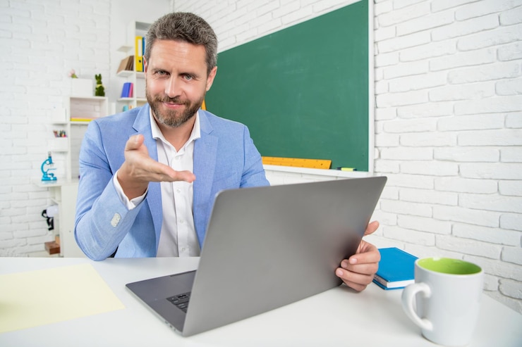 Foto profesor de escuela feliz en el aula con computadora en la pizarra