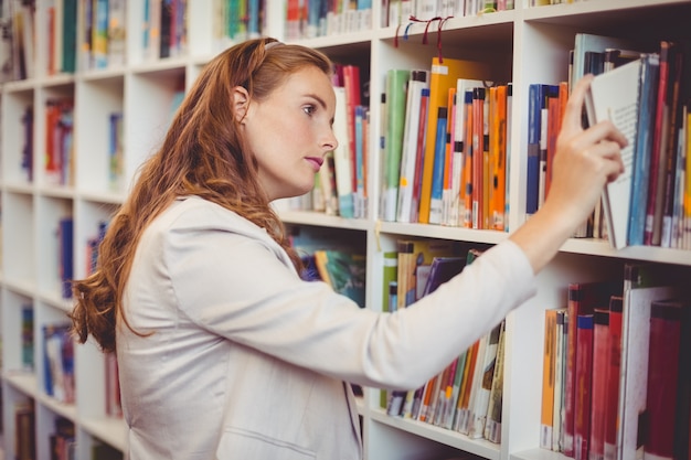 Profesor de la escuela seleccionando un libro de estantería en la biblioteca