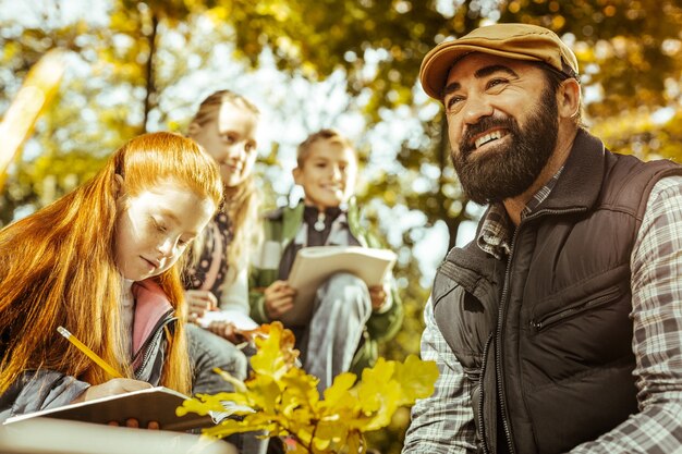 Un profesor feliz y sonriente dando una lección para los alumnos en el bosque en un día soleado