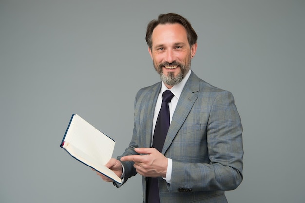 Profesor feliz en traje formal señalar con el dedo en el espacio de copia de conocimiento de fondo gris de libro escolar abierto