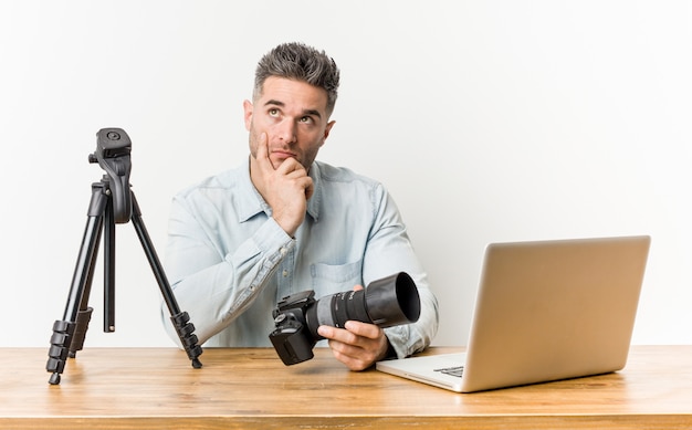 Profesor de fotografía guapo joven mirando hacia los lados con expresión dudosa y escéptica.