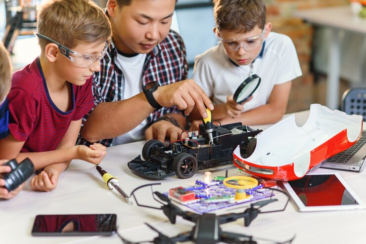 Foto profesor de ingeniería electrónica con jóvenes estudiantes europeos que trabajan junto con un modelo de automóvil controlado por radio. soldadura de alambres y circuitos, experimentos físicos.